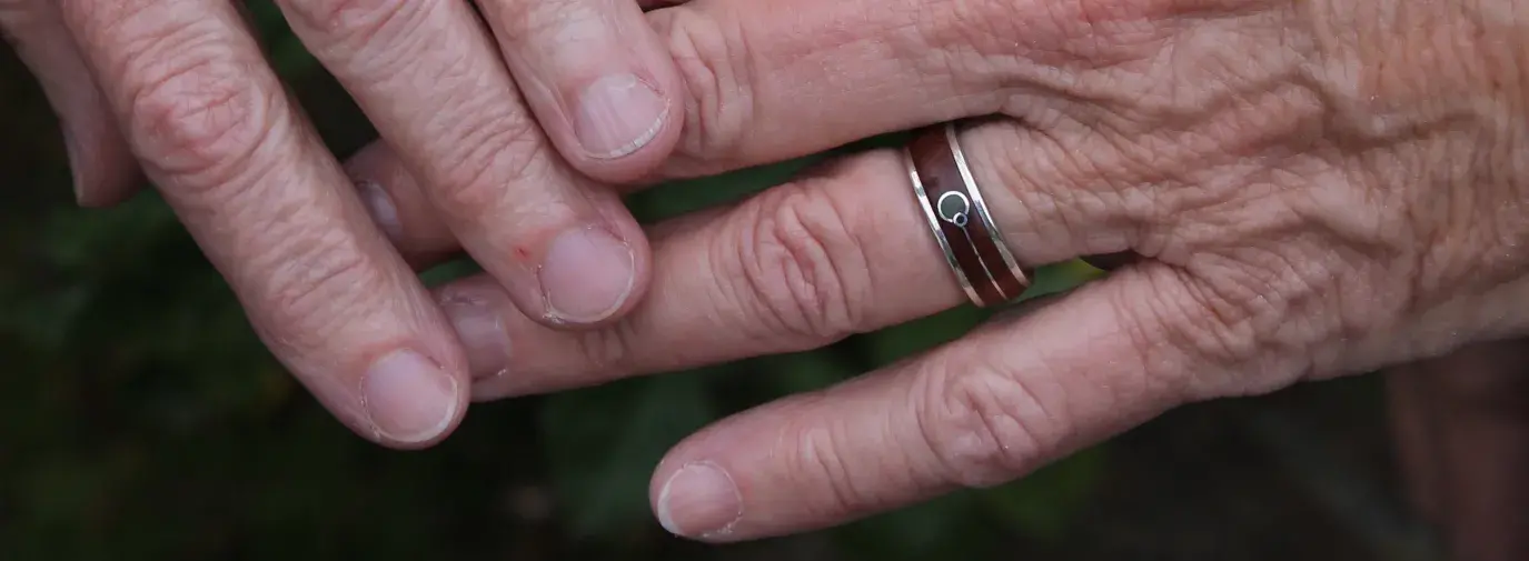 elderly hands wearing natural wood wedding rings and holding a yellow flower